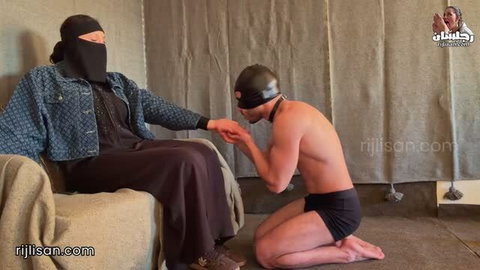 Kneeling male slave worships shoes while dominant woman in niqab slaps him