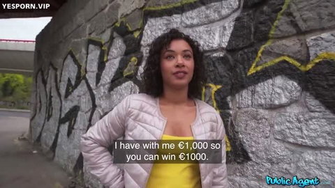 Curly-haired woman in yellow top and pink jacket offers €1000 cash outdoors