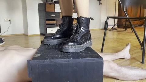 Woman in black Dr. Martens boots trampling naked man on wooden box