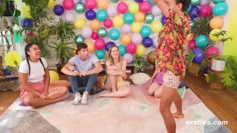 Group of young adults playing a party game on floor with colorful balloon backdrop