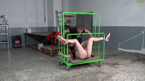 Tied man restrained on metal cart receiving oral sex from dominant male partner