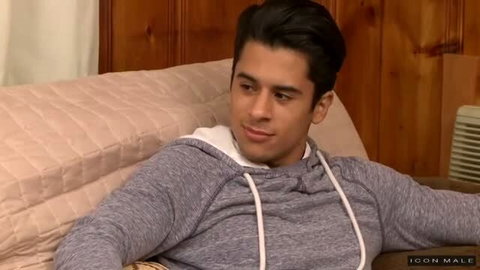 Young man in gray hoodie reclining on bed, looking at camera