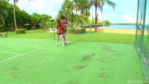 Two women in micro shorts and tops walking on outdoor tennis court