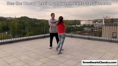 Couple dancing on rooftop terrace, woman in red top and jeans