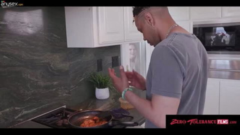Black man in grey t-shirt clapping hands in kitchen near frying pan