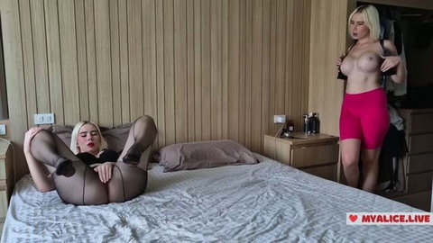 Blonde in sheer black bodysuit poses on bed while busty stepsister in pink shorts watches