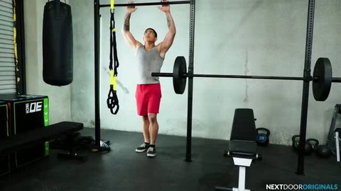 Muscular Asian man doing pull-ups shirtless in gym
