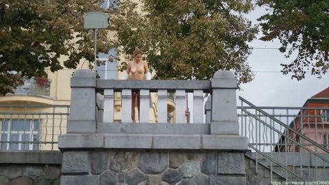 Nude redhead woman with big tits standing outdoors on stone balcony railing