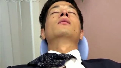 Asian man in suit reclining in dental chair with patterned bandana