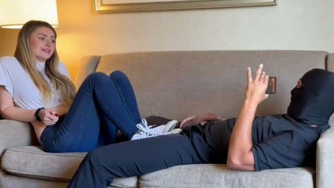 Bratty blonde in jeans teasing man in balaclava on couch