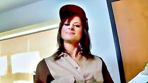 Brunette MILF in tan uniform and hat smiling teasingly in office