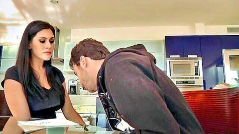 Brunette Latina MILF in black top stands over kneeling hooded man face at her crotch in kitchen