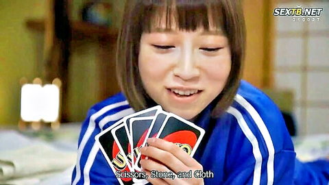 Cute Asian schoolgirl in tracksuit playing UNO cards in dorm on school trip