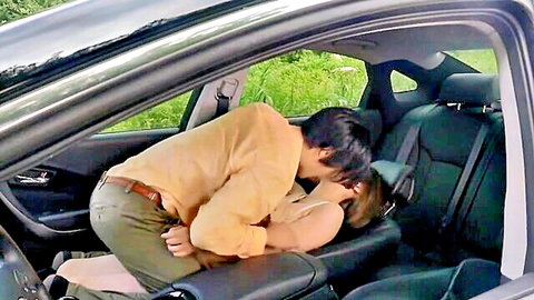 Asian couple in passionate car kiss, man nuzzling woman's exposed chest