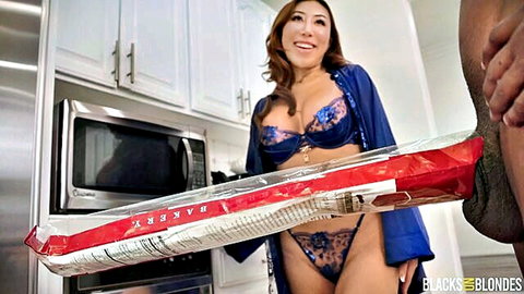 Asian babe in blue lingerie smiles holding long baguette next to thick BBC cock in kitchen
