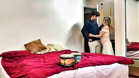 Man intimately hugs blonde woman in lacy white dress from behind in bedroom mirror reflection