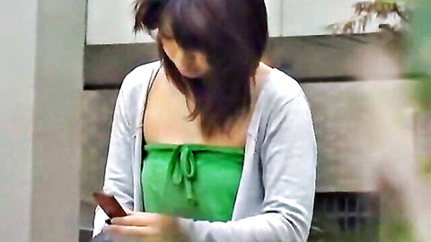 Asian woman in green tube top and white cardigan holding phone outdoors
