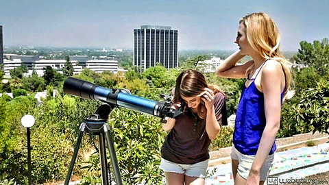 Alexa Grace and Kristen Scott peering through telescope outdoors