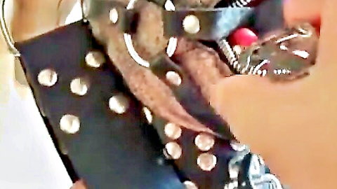 Submissive woman gagged with red ball gag held firmly by gloved hand in studded leather BDSM harness