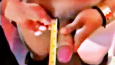 Woman with red nails measuring erect penis using yellow tape, close-up