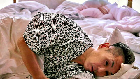 Asian man lying relaxed on bed with open mouth and patterned shirt