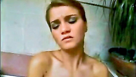 Close-up of short-haired brunette with smoky eyes grimacing in ecstasy, topless in bathroom tub