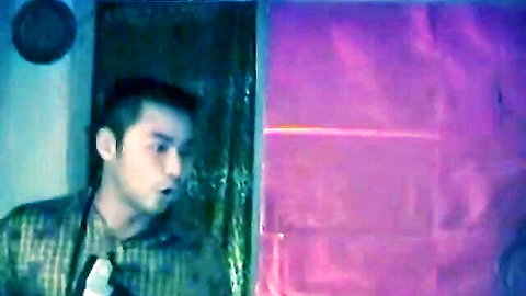 Asian man in checkered shirt with open mouth in dim erotic setting