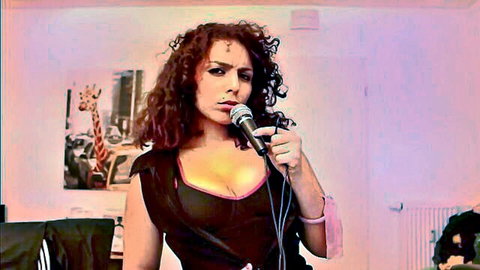 Seductive curly-haired brunette in black top with deep cleavage holding microphone sensually