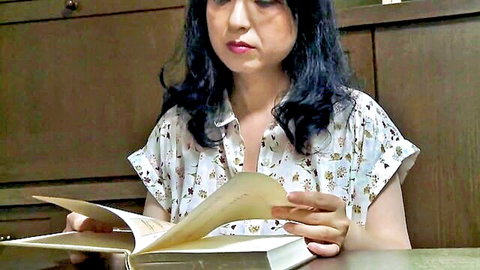 Mature Asian woman in floral blouse reading book, showing cleavage