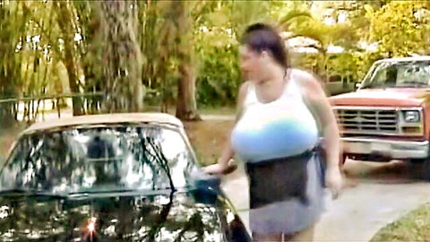 Busty brunette in tight tank top and skirt posing by car outdoors