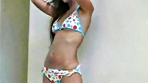 Slim Asian teen in polka-dot bikini posing with arms raised